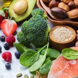 Selection of healthy food for heart, salmon fish avocado olive oil pumpkin seeds nuts broccoli green spinach berries on a white rustic table